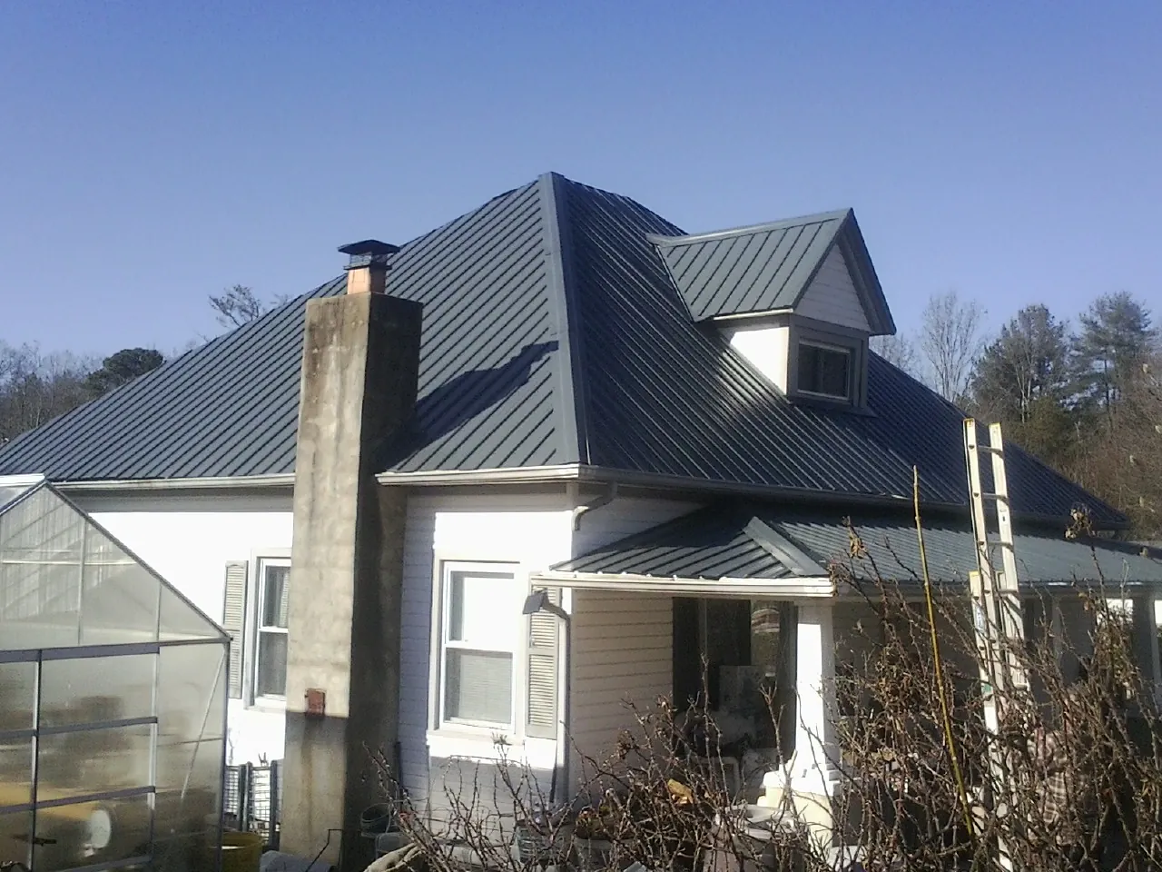 Dark blue standing seam metal roof on a white farmhouse with dormer — Slate & Tile Roof Repair by Roofing Brothers in Mount Sinai