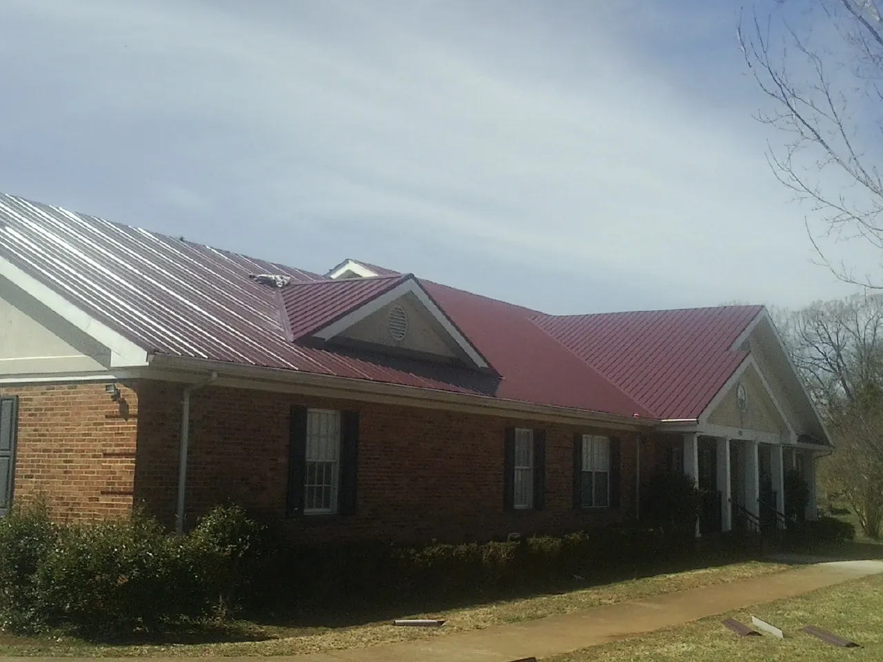 Red metal roof with gabled entries on a long brick building, from a Hail Damage Roof Repair job in Mount Sinai