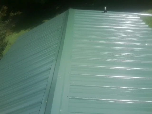 New green metal panels meeting at the ridge of a roof — Flat Roof Repair work by our crew in Mount Sinai