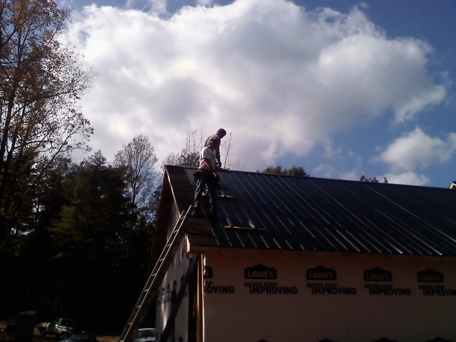 Roofer fastening dark metal panels high against a cloudy sky, from a Roof Inspection job in Mount Sinai