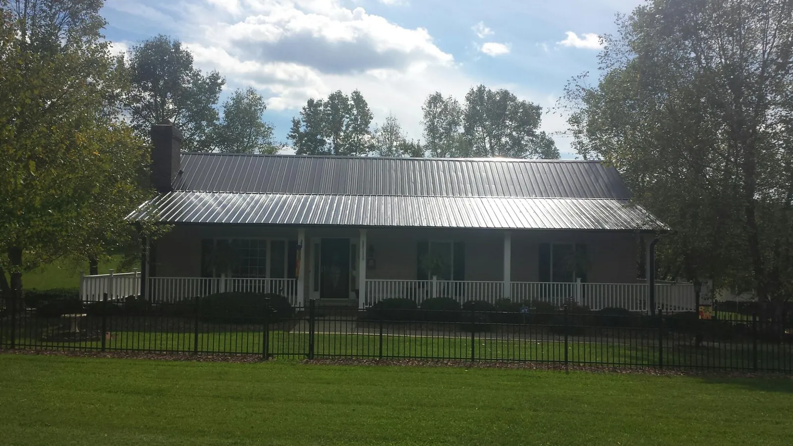 Gray metal roof on a brick ranch with a full width front porch — Gutter Guard Installation work by our crew in Mount Sinai