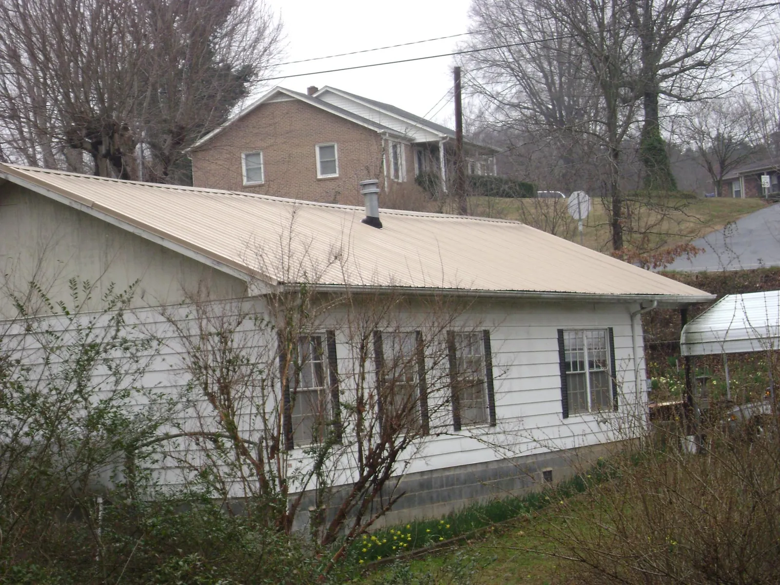 Tan metal roof on a white sided house set into a hillside — Commercial Roofing by Roofing Brothers in Mount Sinai