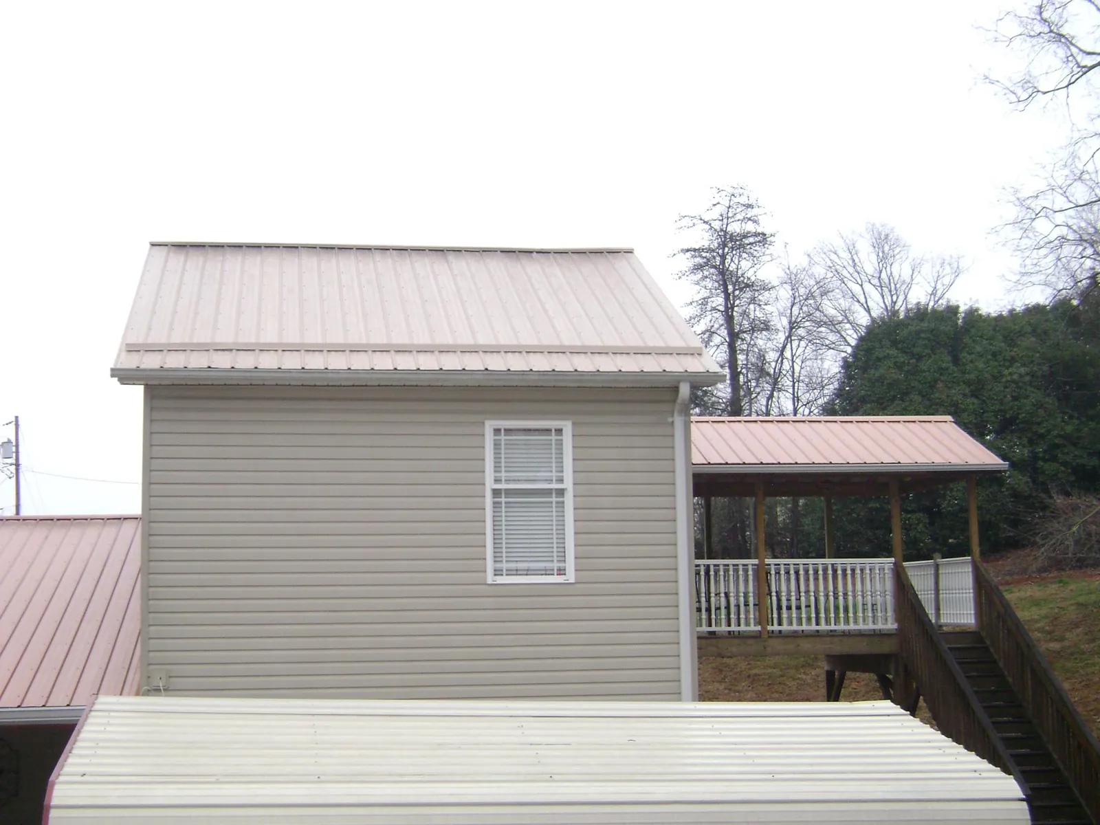 Tan metal roofs on a two story addition and attached porch, from a Roof Replacement job in Mount Sinai
